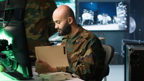 oficial militar recibiendo una llamada telefónica mientras miraba archivos de inteligencia