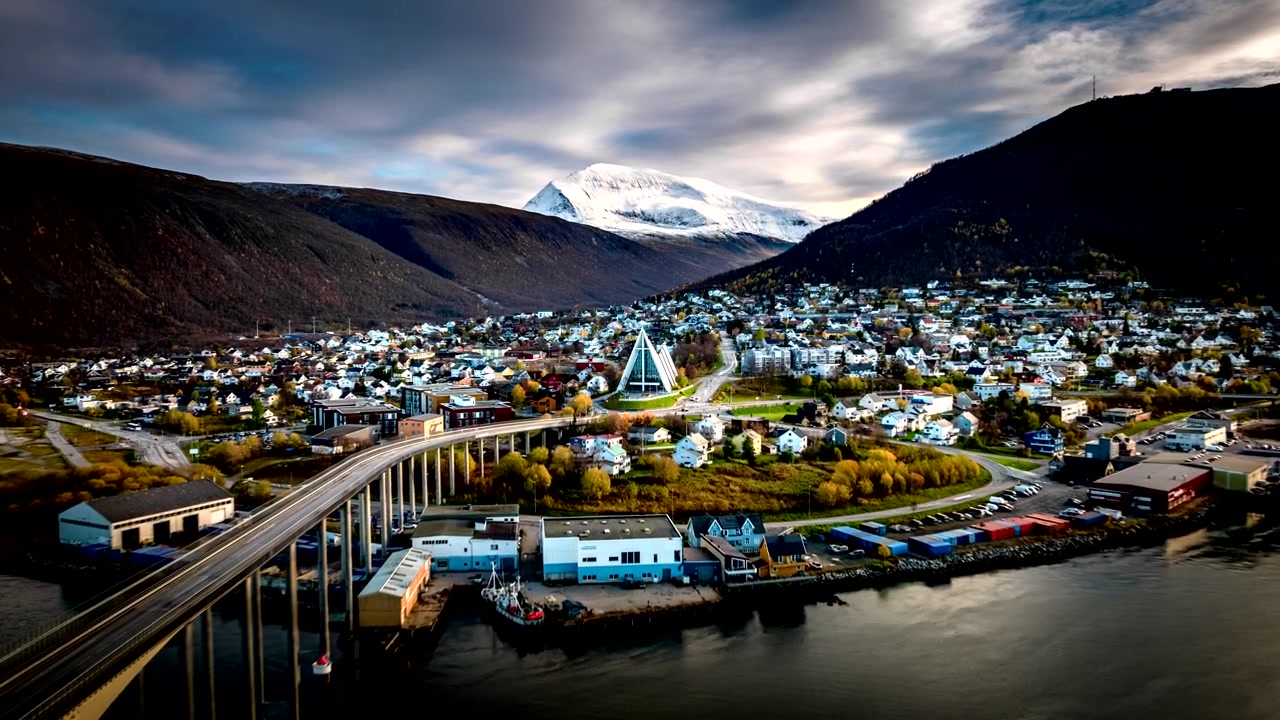 Ikonische moderne Kirche, die Tromsdalen-Kirche, und Stadtverkehr in der Dämmerung in Tromsø, Norwegen. Hyperlapse, Luftaufnahme vorwärts.