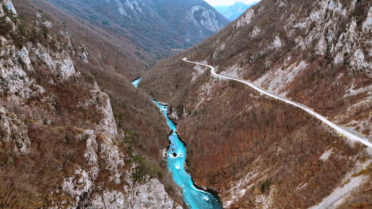 Strada tortuosa lungo il fiume turchese nel canyon del Montenegro. Vista aerea di una strada asfaltata serpentina che segue un fiume blu brillante attraverso un profondo canyon roccioso in Montenegro