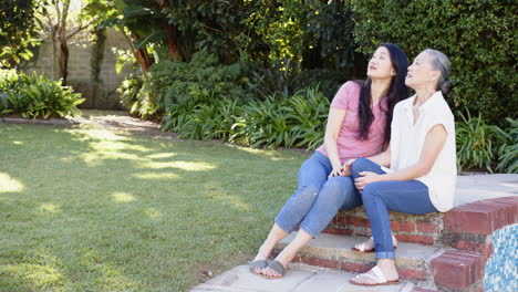sitting on steps, asian grandmother and granddaughter enjoying outdoor time together in garden