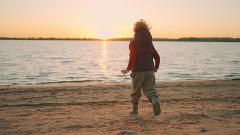 playful curly child is running on river shore in spring sunset time happiness and childhood moments