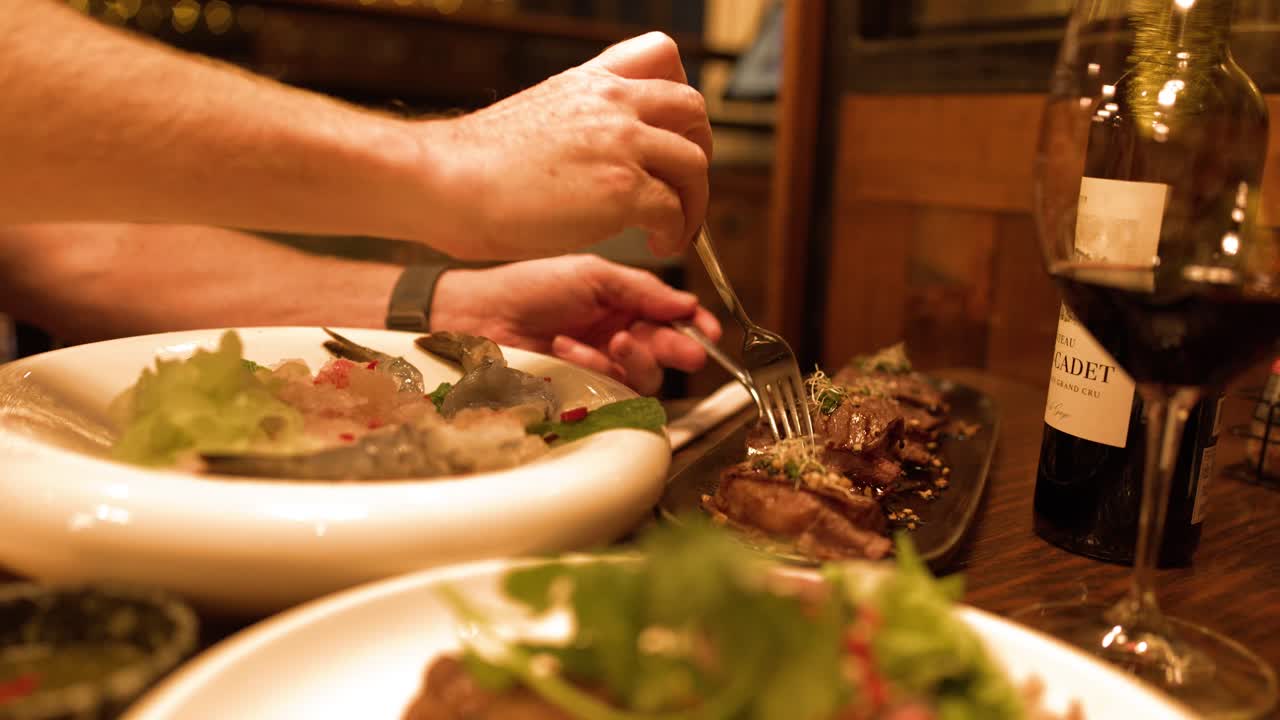 A person uses a fork to pick up steak during a romantic fine dining dinner
