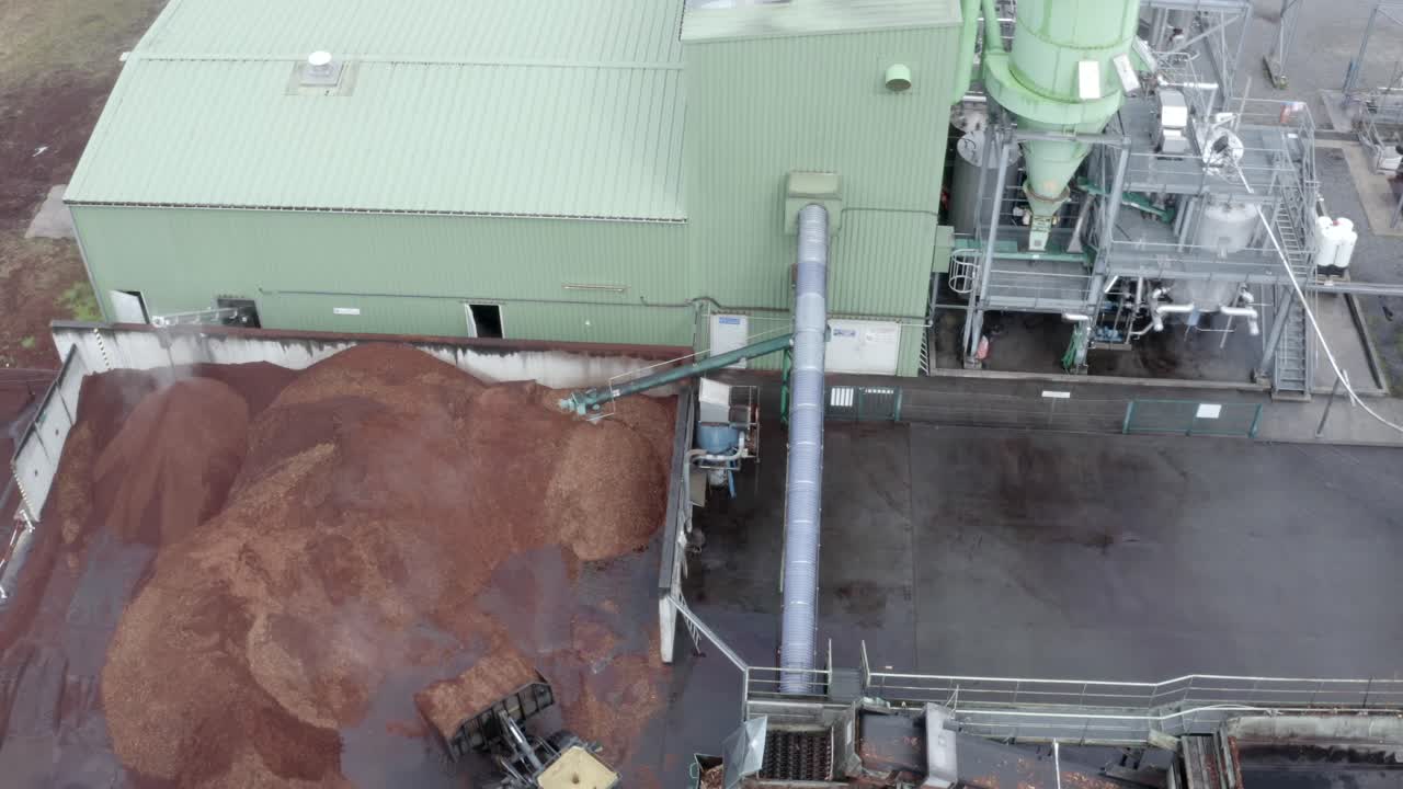 Aerial circling view of loader moving wood chips at DRT industrial plant, processing equipment visible, Veille-Saint-Girons, France