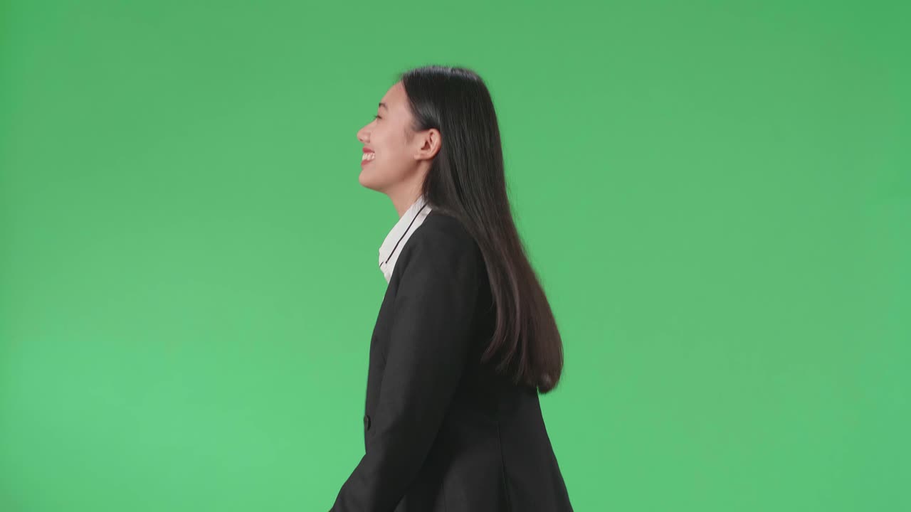Side View Of A Smiling Asian Business Woman Walking Through Green Screen In The Studio