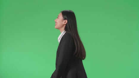 side view of a smiling asian business woman walking through green screen in the studio