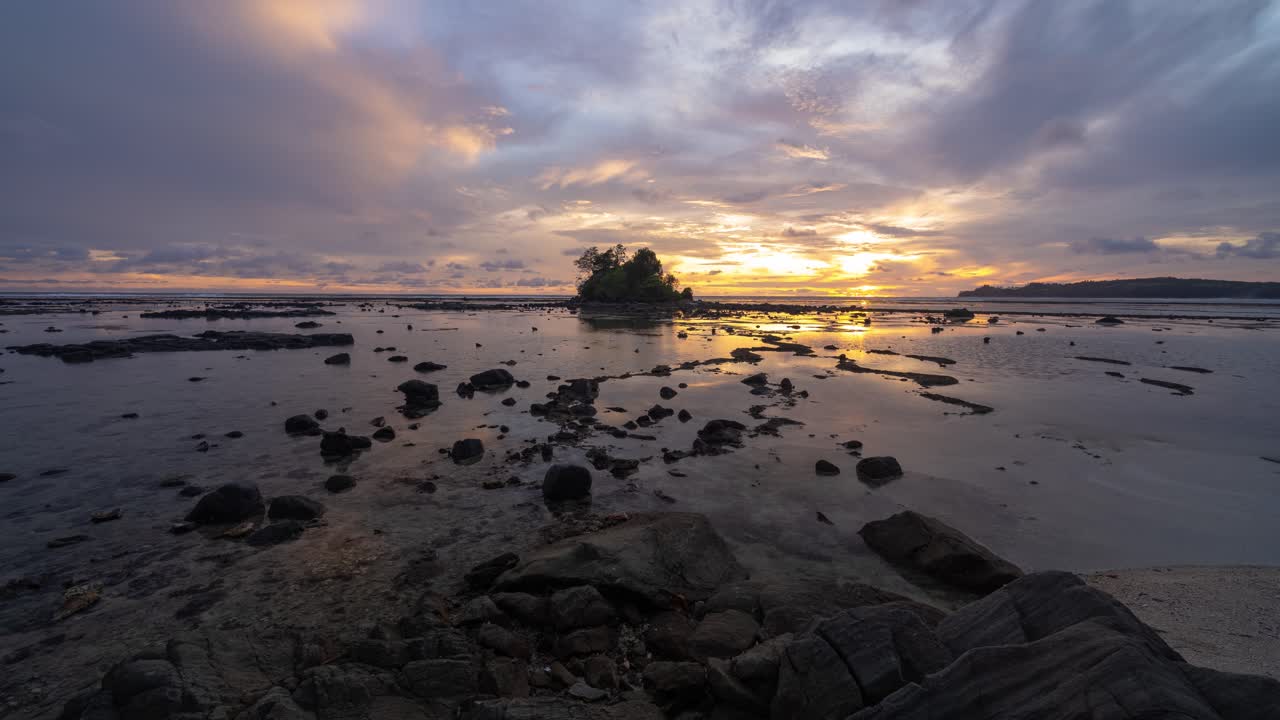 Sunset over a rocky tropical beach with a distant island and a person observing
