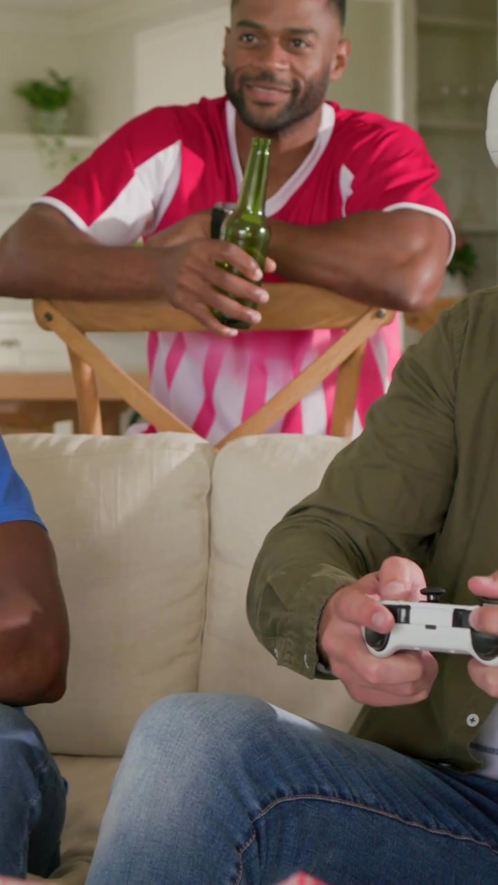 Vertical video: Leaning man in red watching VR game at home, shifting and sipping green beer bottle