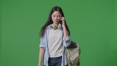 초록색 스크린 배경 스튜디오에서 는 동안 스마트폰으로 이야기하는 배을 가진 아시아 십대 소녀 학생