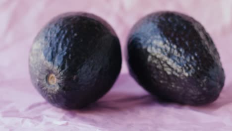 tres aguacates se colocan sobre una tela rosa, dos manos de niña entran y toman una muy suavemente, escena en cámara lenta y luz natural-1