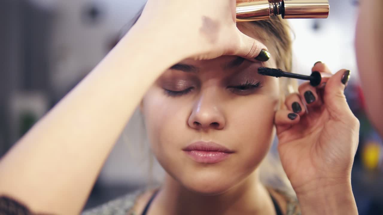 Close Up view of professional makeup artist's hands applying mascara on eye lashes of a young attractive model. Slow Motion shot