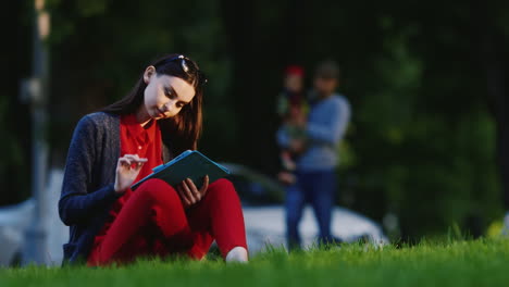 mujer elegante sentada en el césped en el parque disfrutando de la tableta en el fondo la gente camina hd