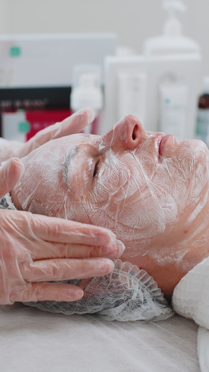 Estetista che applica maschera di crema idratante peeling sul viso di una giovane donna per reidratare la pelle del viso