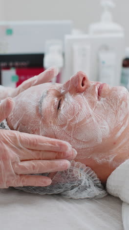 beautician applying peeling moisturizing cream mask on young woman face for rehydrate face skin