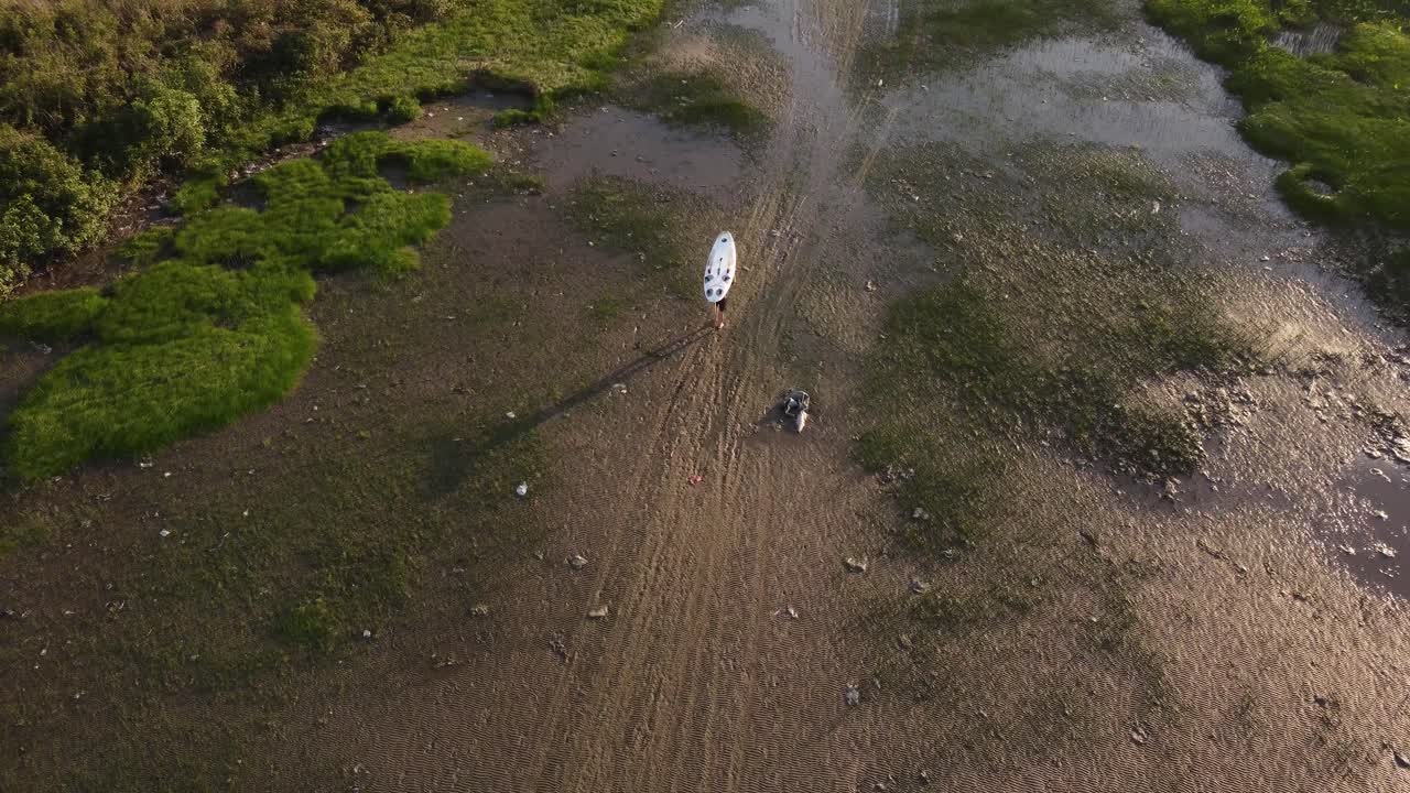 toma aérea de un surfista que lleva una tabla de surf sobre la cabeza después de surfear en el río de la plata al atardecer