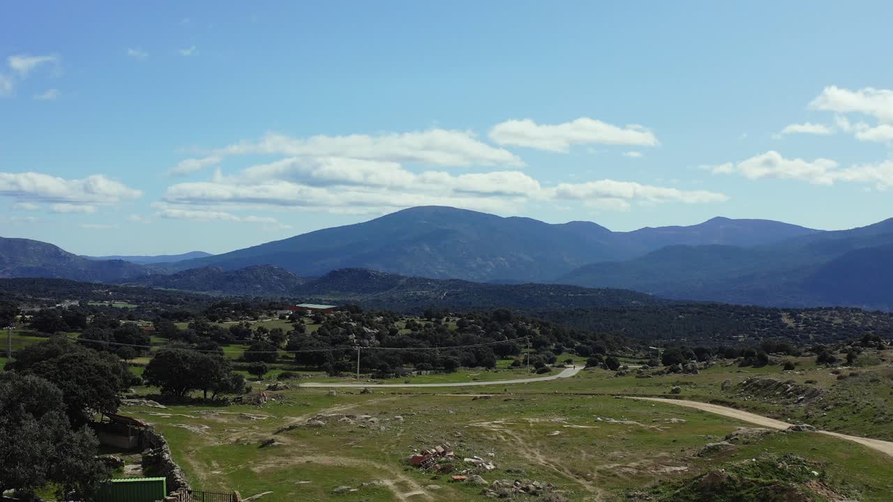 al volar hacia adelante sobre los techos rojos de las casas pequeñas en un día soleado, se puede ver el pasto de robles con varios caminos rurales y las montañas en el fondo en el valle de iruelas, ávila, españa.