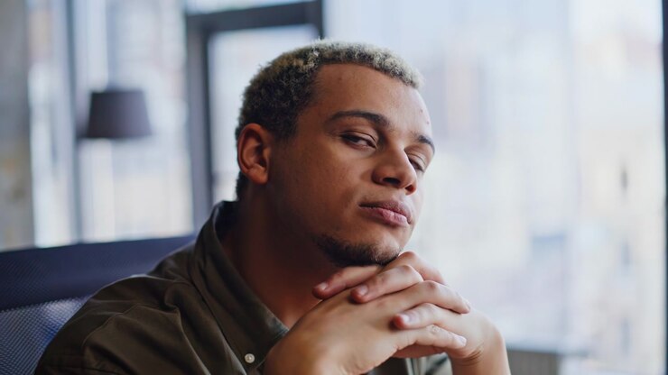 Contemplative man resting chin on hands looking out window. Dreamy portrait