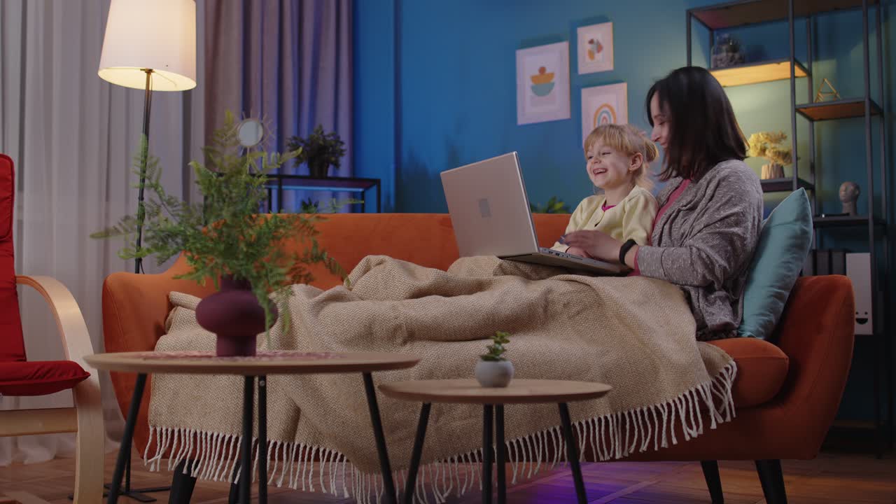 Mother and small child daughter kid study at laptop watching funny movies relaxing lying on sofa