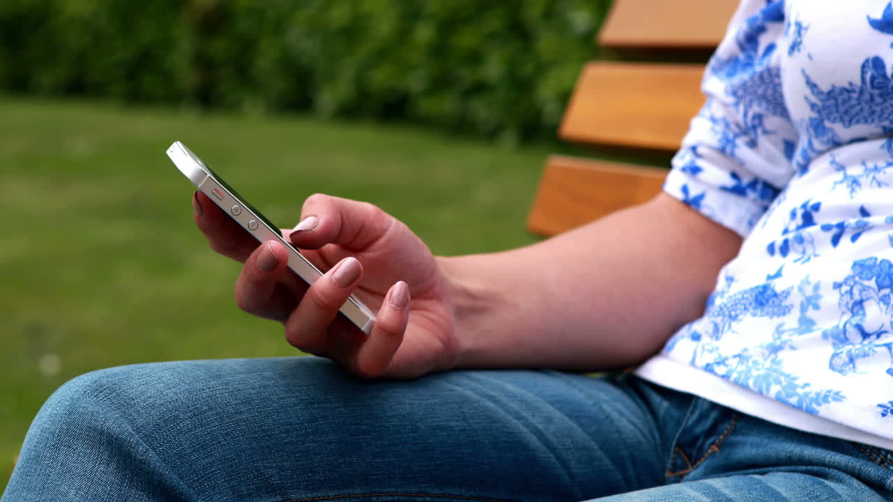 Donna seduta su una panchina del parco che scrive messaggi
