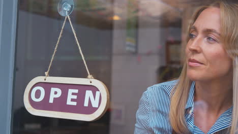 female owner or staff inside shop or cafe turning round sign from closed to open