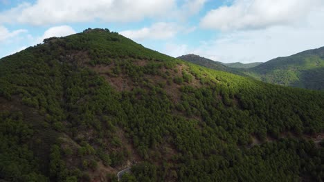 Sun-shines-through-clouds-on-forest-covered-mountains-of-Spain,-aerial-view