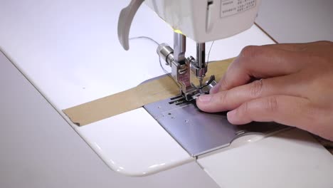 un primerísimo plano en el dedo empujando la tira de tela gruesa con patrones en forma de triángulo a través de la máquina de coser para coser el borde exterior