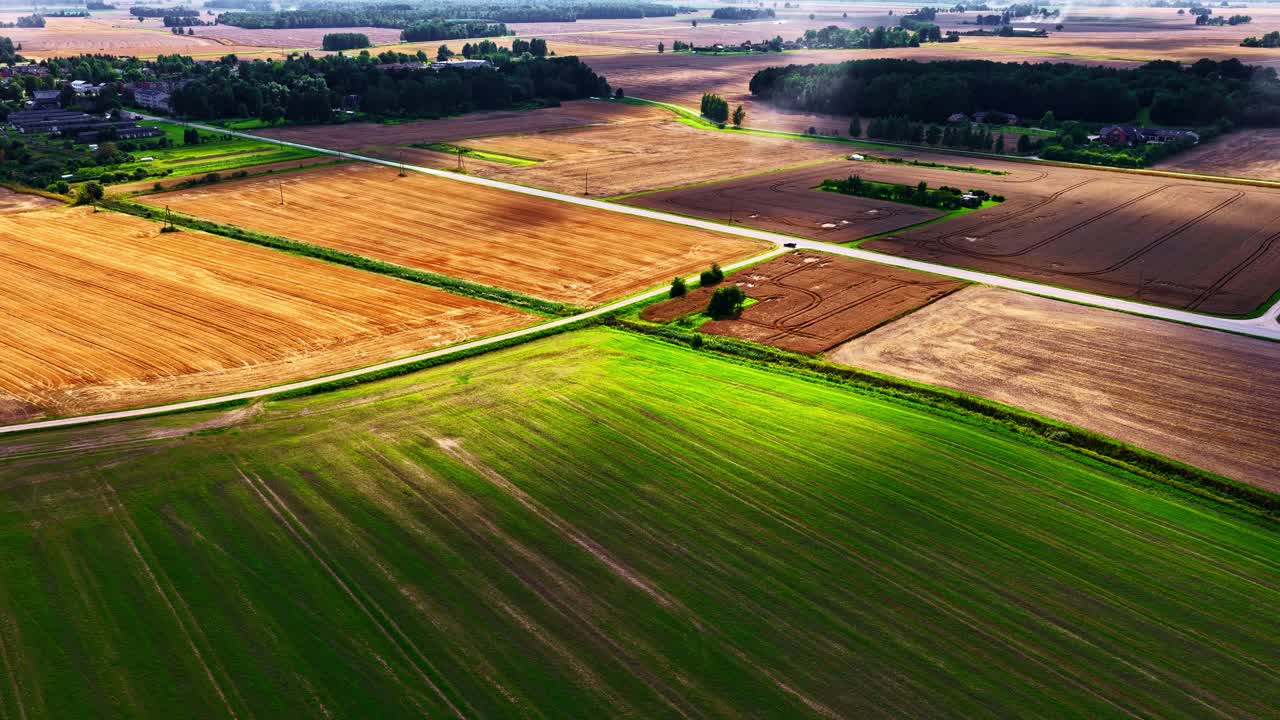 Aerial drone view descends over a patchwork of green and golden agricultural fields after crop harvest in the beautiful rural countryside of Latvia