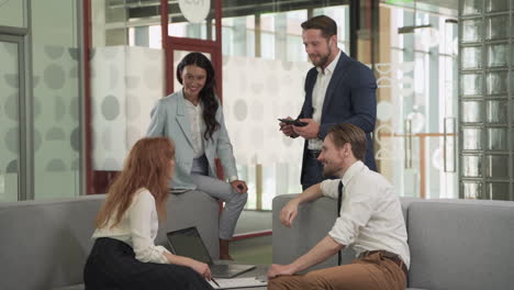 a business working group consisting of two women and two men have a relaxed meeting in the armchairs in the common area of the offices 3