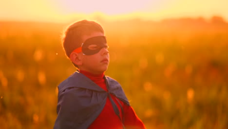 a child in the costume of a superhero in a red cloak runs across the green lawn against the backdrop of a sunset toward the camera.