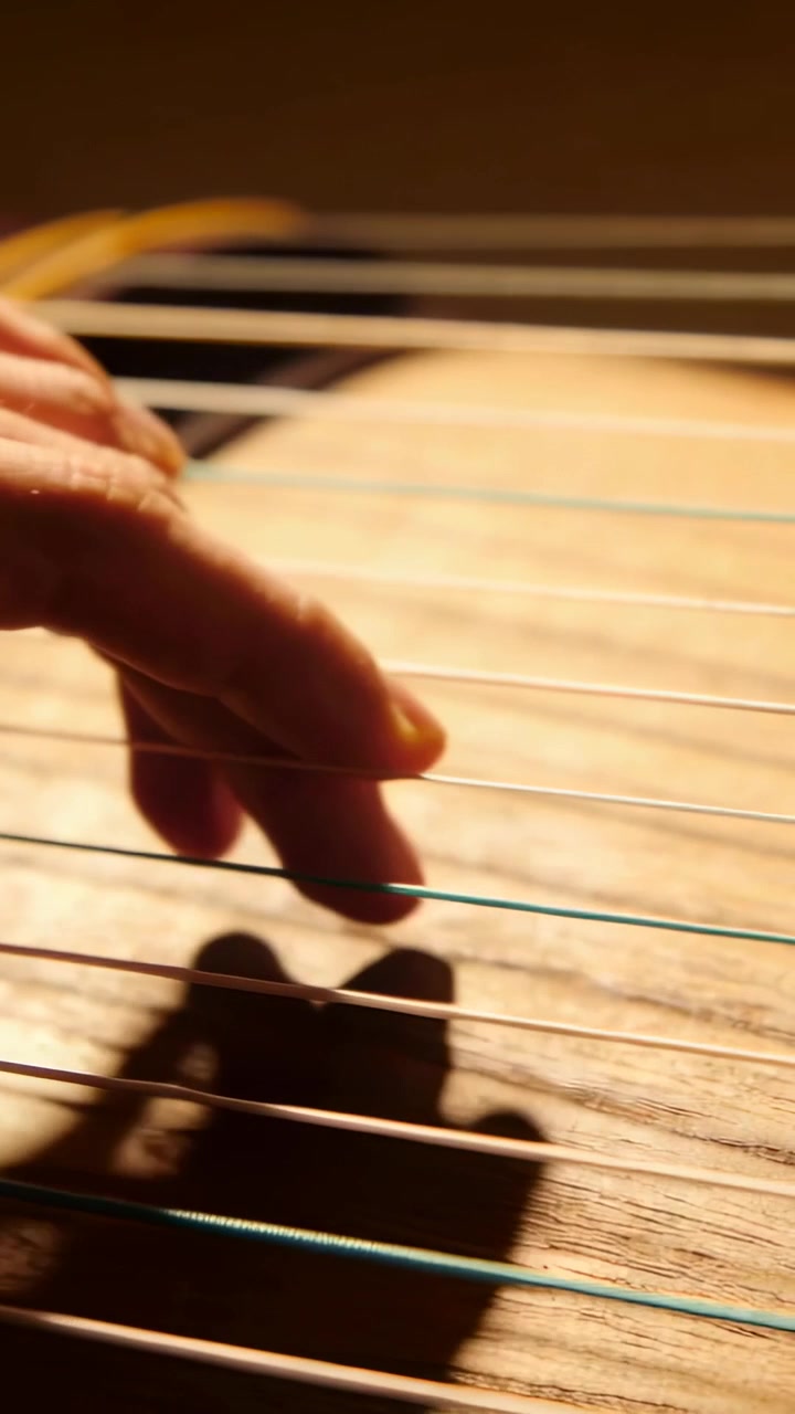 Vertical video: Hovering hand moving down to pluck guitar strings in music room, creating melody