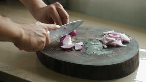 close-up shot of amateur chef's hands slicing red onions on a wooden chopping board.
