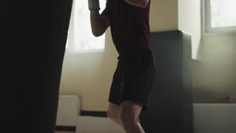 el deportista entrena la patada redonda en la bolsa de boxeo en el gimnasio. el maestro de artes marciales hace ejercicio con equipos pesados en el club deportivo en cámara lenta. ocio saludable