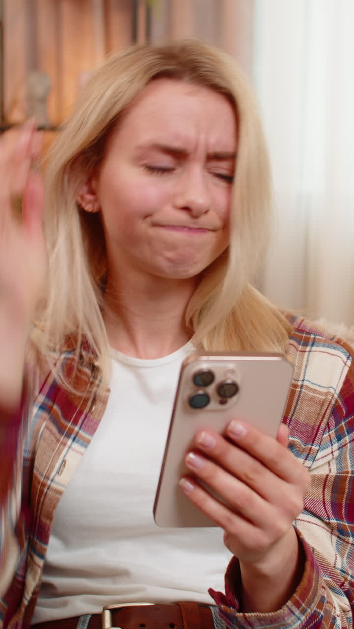 Young adult woman reacting angrily to bad comments and online game loss on smartphone at home sofa