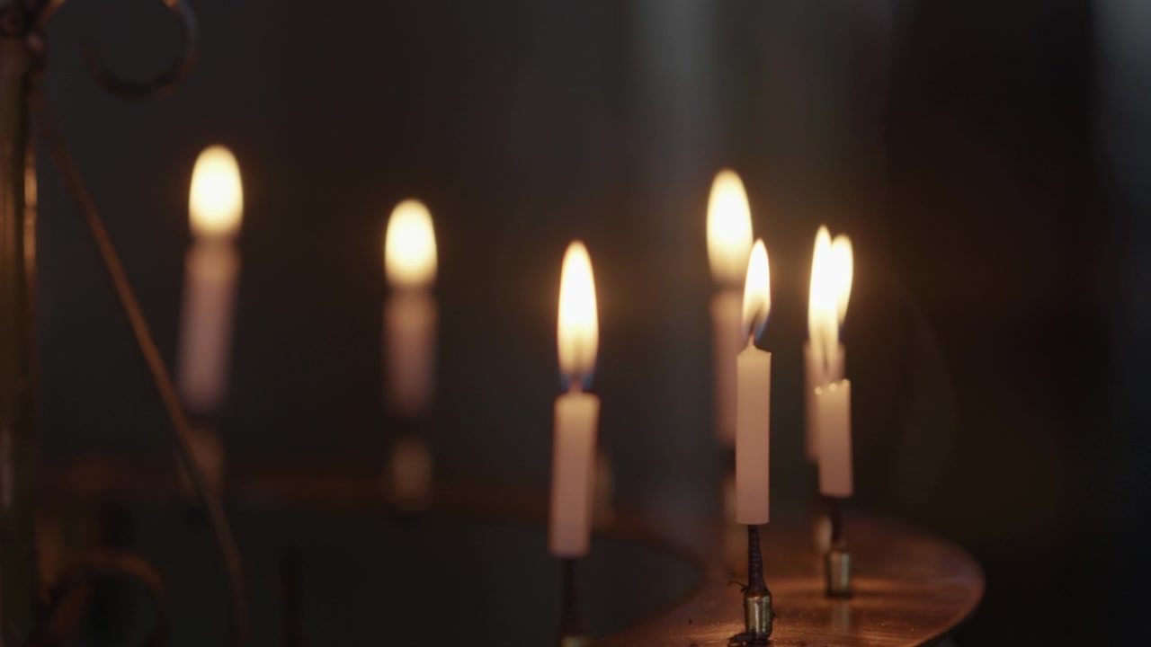 Fila di candele sottili accese che brillano su un supporto di ottone nella calda oscurità di un tempio giapponese