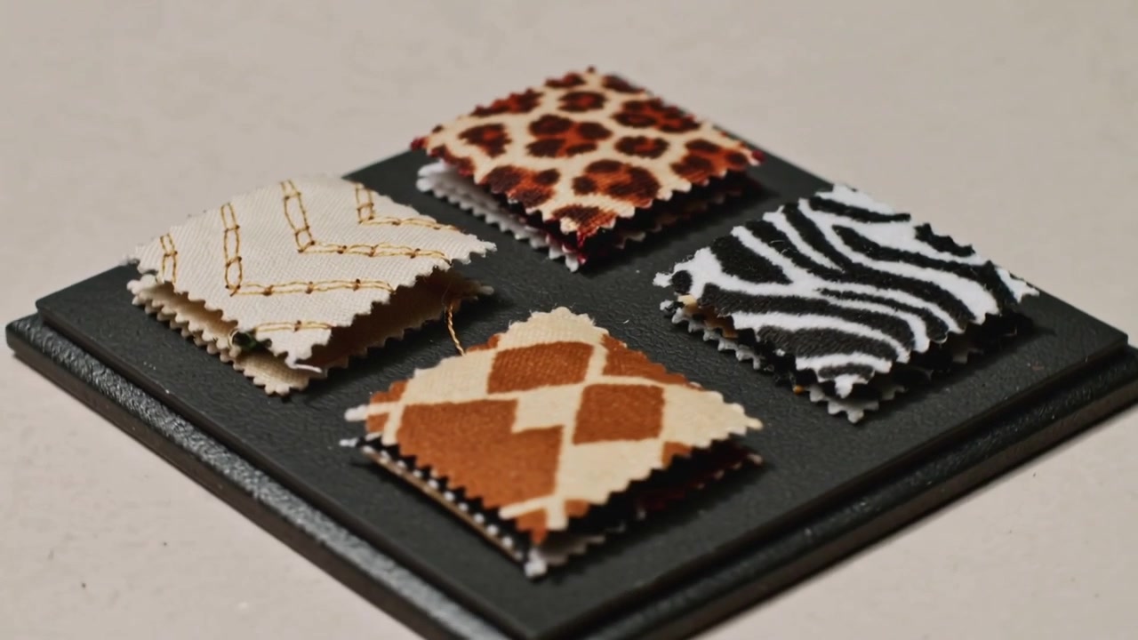 Panning camera revealing 4 stacked fabric swatches on beige table, showing patterns and gold thread
