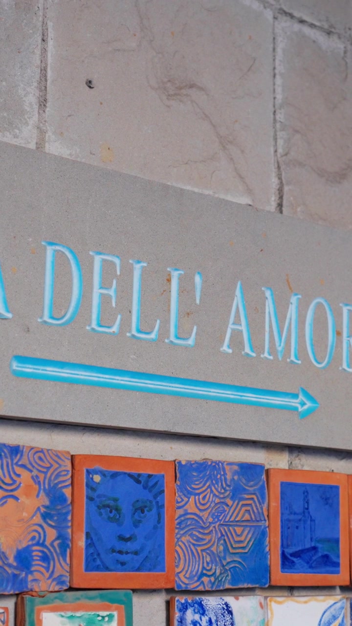 Close-up van het Via dell'Amore-bord met blauwe pijl boven decoratieve keramische tegels