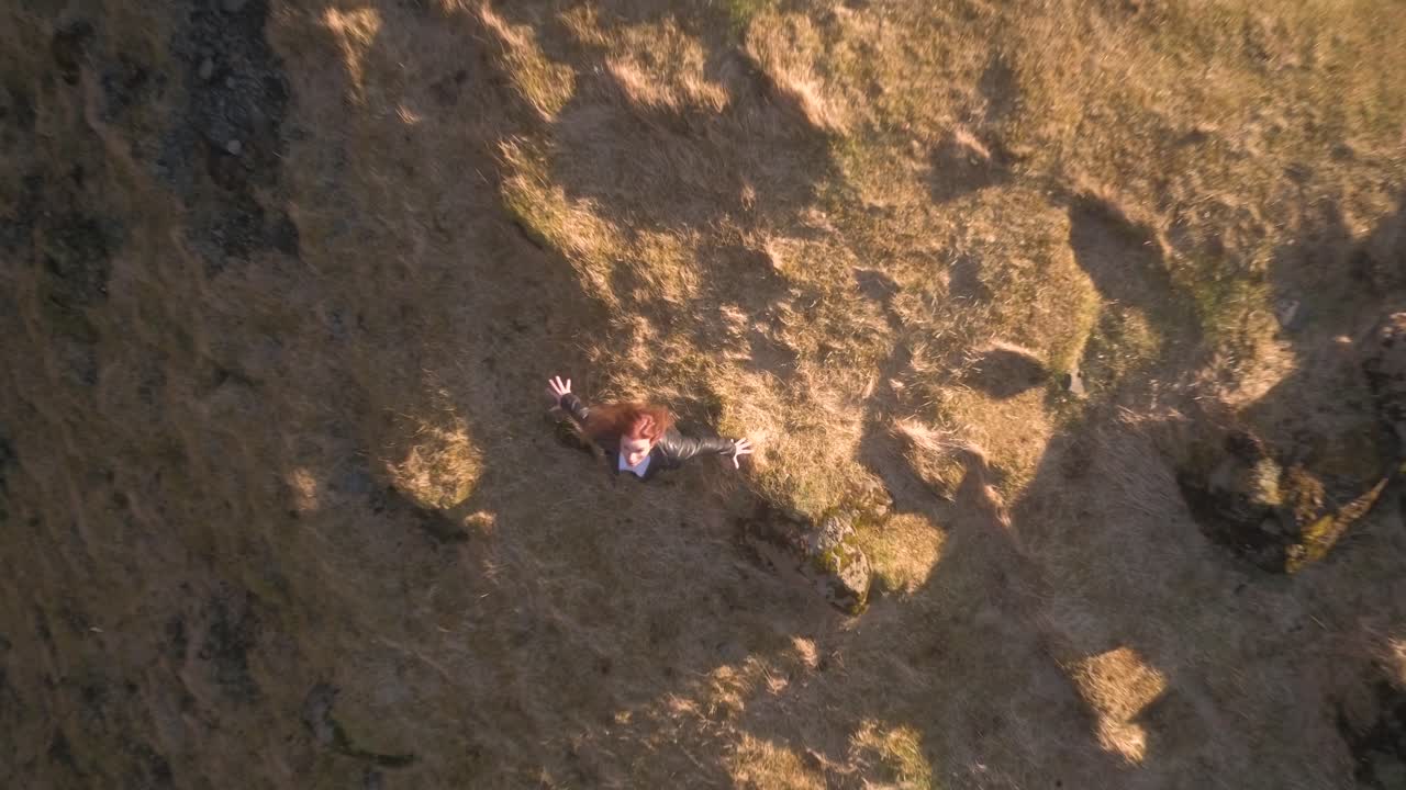 Frightened woman with open arms on cliffs edge. Aerial birds eye, rising