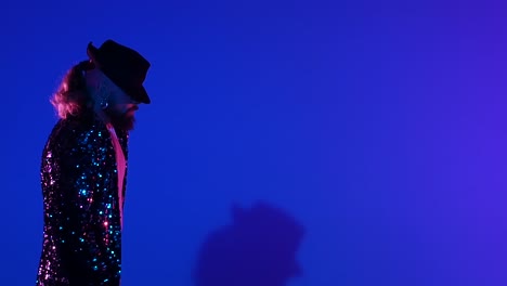 man in sequin jacket and hat on blue background with neon lighting