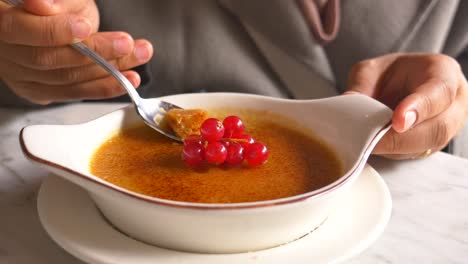 person enjoying delicious creme brulee with red berries