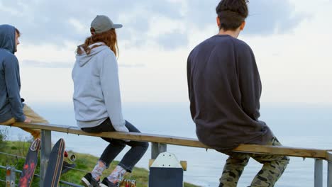 Rear-view-of-young-caucasian-skateboarder-with-skateboard-sitting-on-railing-at-observation-point-4k