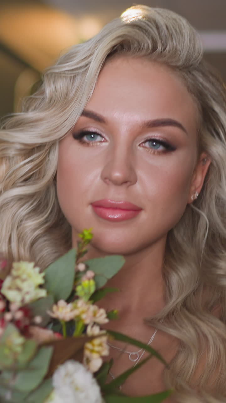 Stylish woman bride with festive hairstyle holds arranged fresh flowers bouquet walking along light hallway of modern hotel closeup slow motion