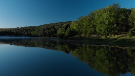 early morning low drone shot over glossy lake and some fog-2