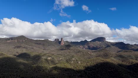 cloud shadows drift over rugged volcanic peaks and forested hills in warrumbungle national park, under bright daylight with a wide, steady camera view