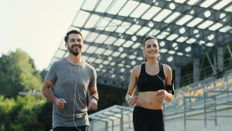 Vista-De-Cerca-De-Una-Pareja-De-Jóvenes-Corredores-Corriendo-Juntos-Escuchando-Música-Con-Auriculares-En-El-Estadio-En-Una-Mañana-De-Verano-1