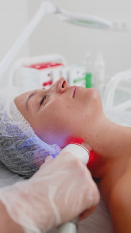Beautician makes woman rf lifting cosmetology procedure of face and neck area collagen mask at spa