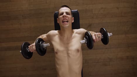 un hombre sin camisa haciendo press de banca en un gimnasio interior - vista superior