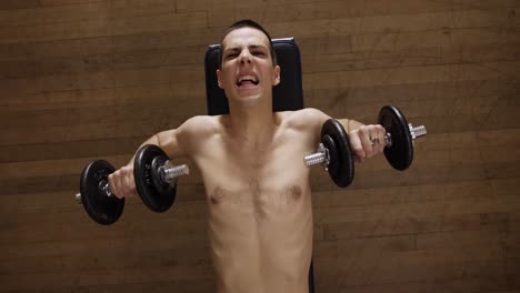 a shirtless man doing bench press in an indoor gym - top view