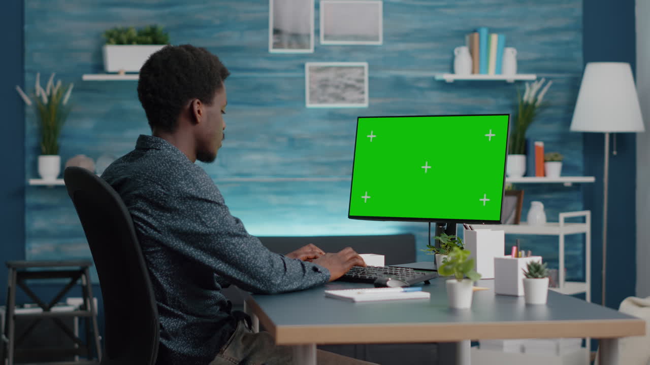 Black man typing and using personal computer with mock up chroma key display
