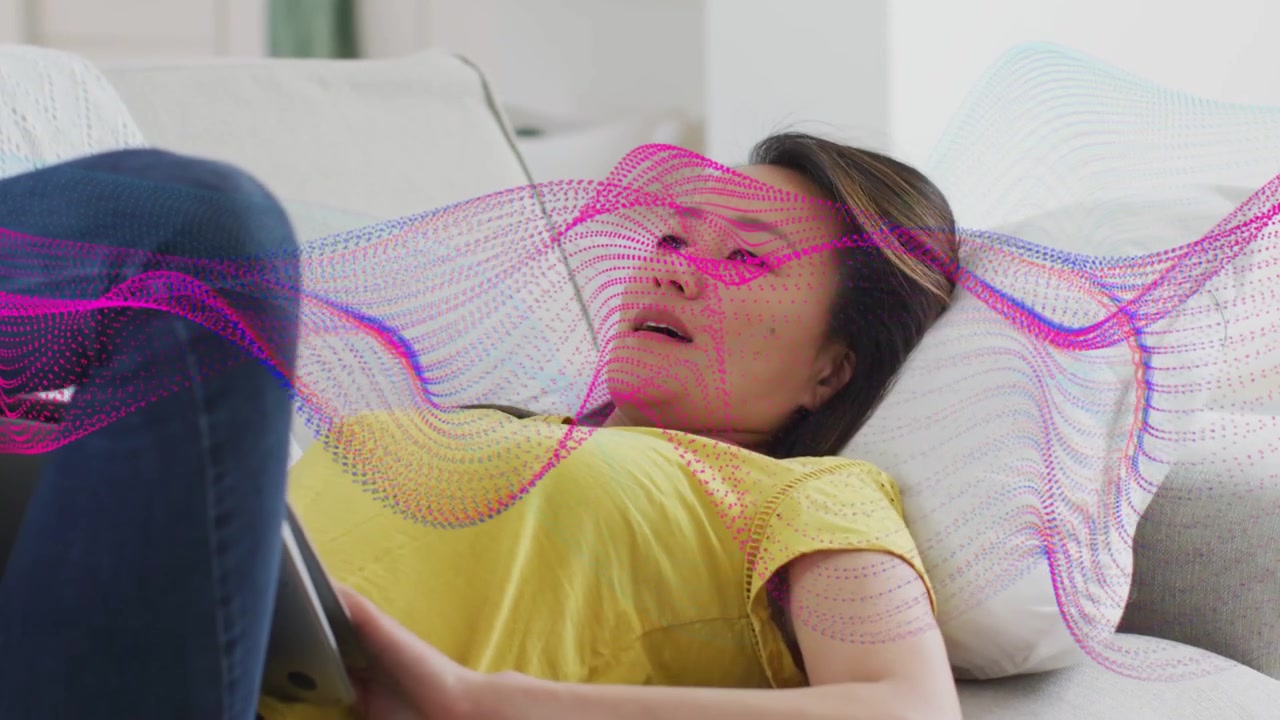 Donna sdraiata sul divano che osserva una forma d'onda del tablet sovrapposta al busto in una demo tecnologica, mentre si aggiusta e sorride.