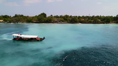 Indonesian-Tour-Boat-Cruising-Along-Gili-Islands-Coastline-on-Sunny-Day--Aerial-Approaching-to-Tropical-Turquoise-Beach