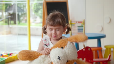 Fröhliches-Kleines-Verspieltes-Mädchen,-Das-Mit-Einem-Spielzeug-Teddybär-Spielt,-Blickt-Mit-Einem-Breiten-Lächeln-In-Die-Kamera